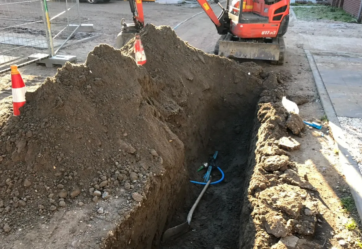 Minigraver naast een open sleuf in een woonstraat